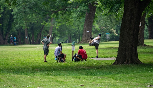 Several people gather around a disc golf tee while one of them throws a driver