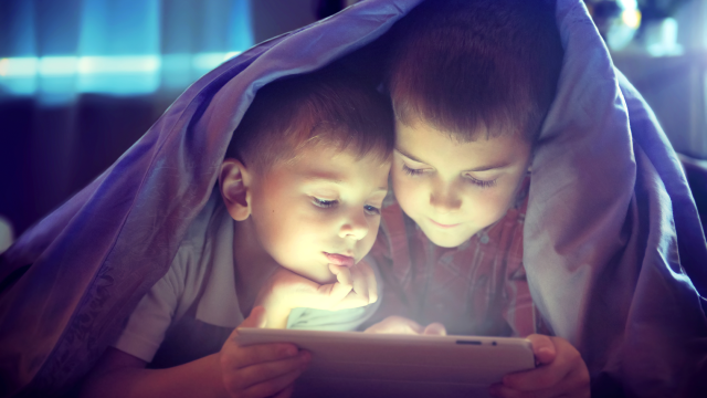 Boys enjoy reading a tablet under the covers at night time