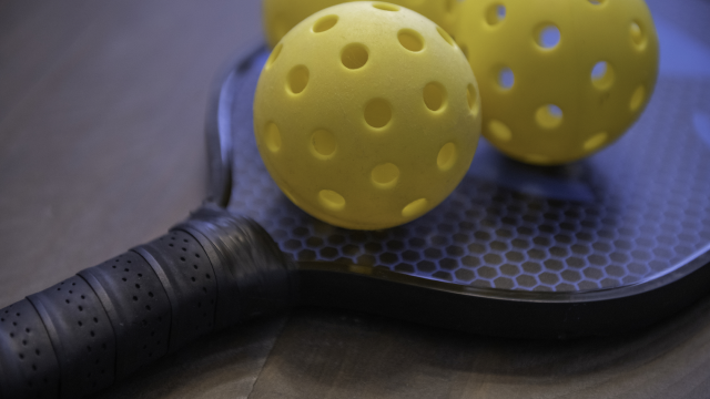 Pickleball paddle on wood surface with 3 plastic balls