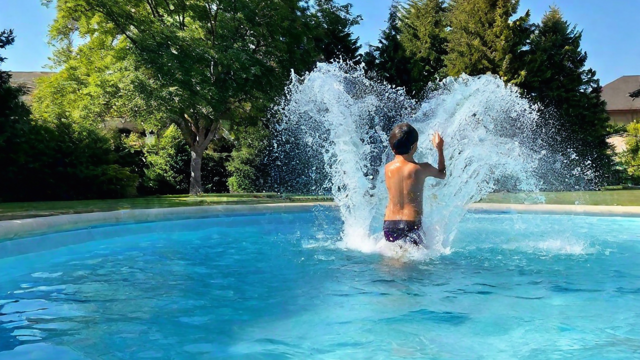 A young boy in black swimming trunks splashing water forward in a pool.