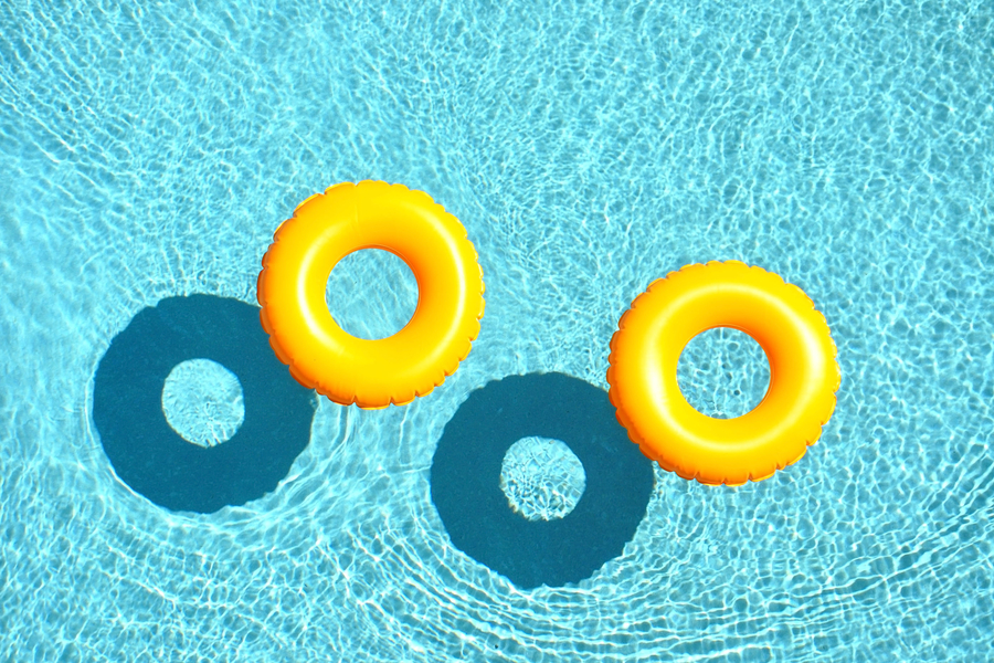 Two bright orange innertubes float in the shimmering waters of a swimming pool.